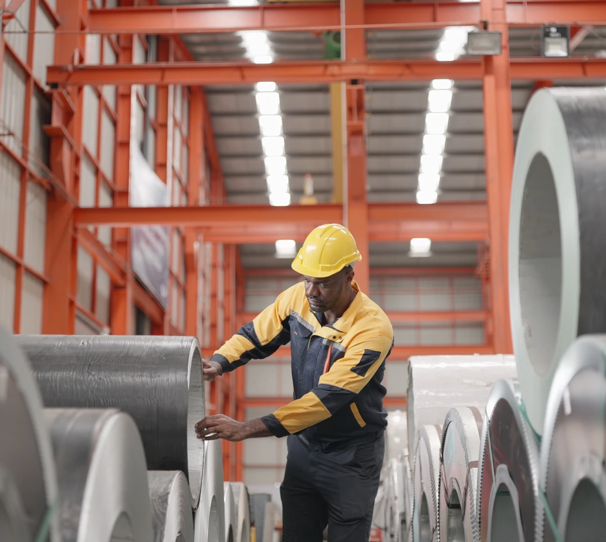 Worker inspecting metal rolls in warehouse.