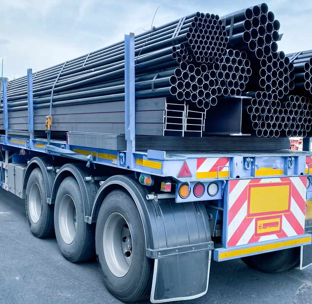 Truck carrying stacked metal pipes on road.