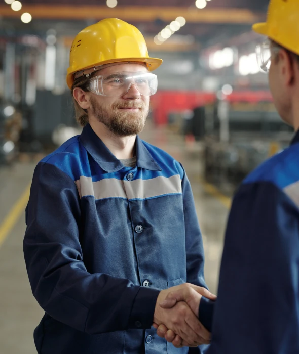 Two workers shaking hands in a factory.